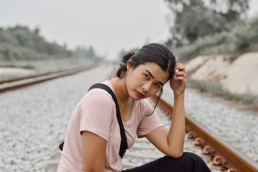 一位年轻细心的少数民族女性坐在铁路边，仰望天空，手抚头发，侧脸看向镜头