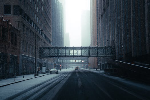 Moody winter scene of a snow-covered street in downtown Minneapolis with skyscrapers and a pedestrian bridge.