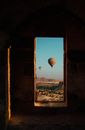 Doorway of aged building with air balloons flying in blue sky over rough terrain