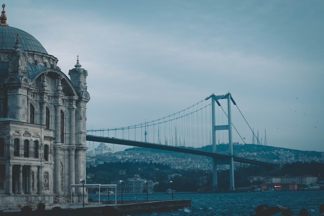 Long metal Bosphorus Bridge connecting Europe and Asia with aged stone cathedral on embankment