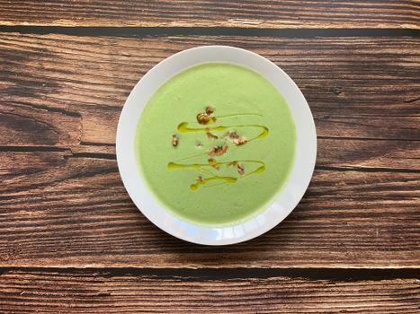 Top view of bowl with tasty healthy broccoli cream soup with walnuts and olive oil served on wooden table