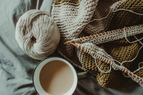 Free From above of cup of hot coffee placed on bed with handmade knitted plaid with needles and wool yarn Stock Photo