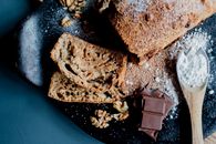 Top view of yummy banana bread with walnuts served on plate with chocolate bars and spoon of sugar powder