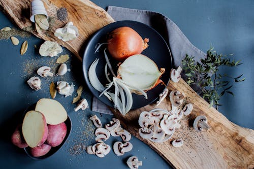 From above of chopped mushrooms scattered on table near plates with fresh onions and sweet potatoes