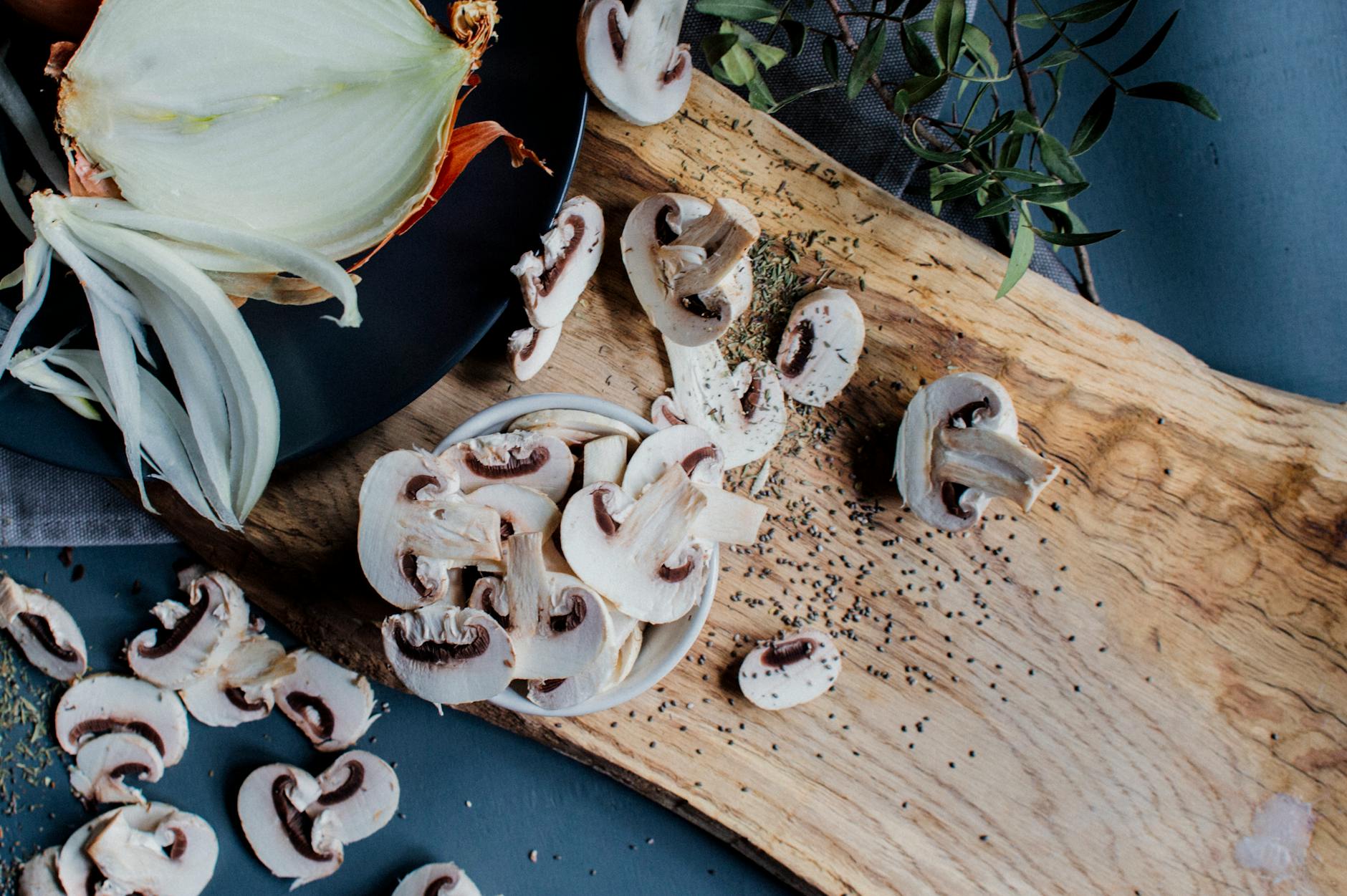 Uncooked mushrooms and onion placed on table with fresh rosemary