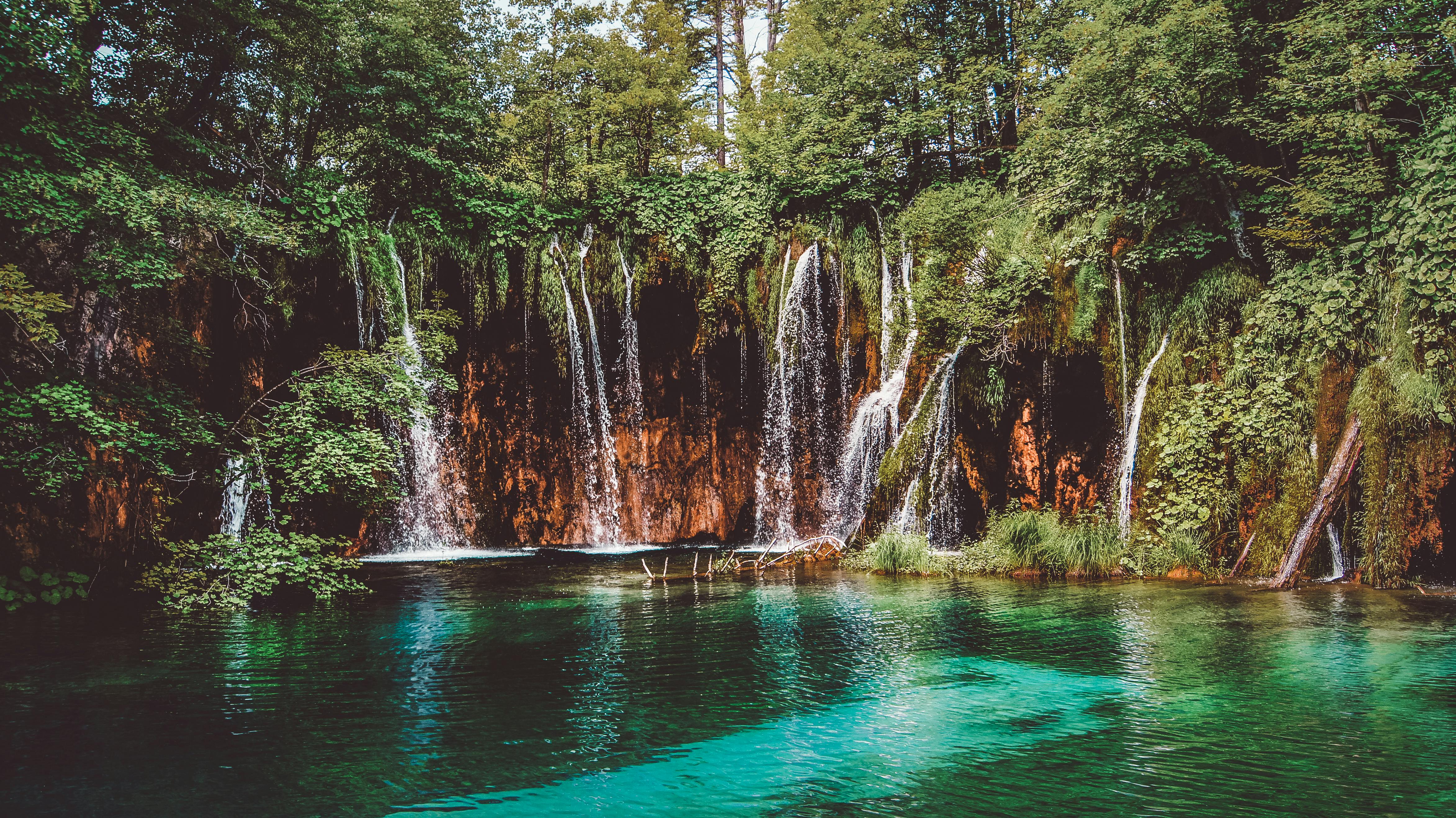 amazing waterfall flowing through rocky cliff with green trees on sunny day