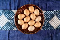 An overhead view of organic eggs in a woven basket placed on a blue patterned cloth.