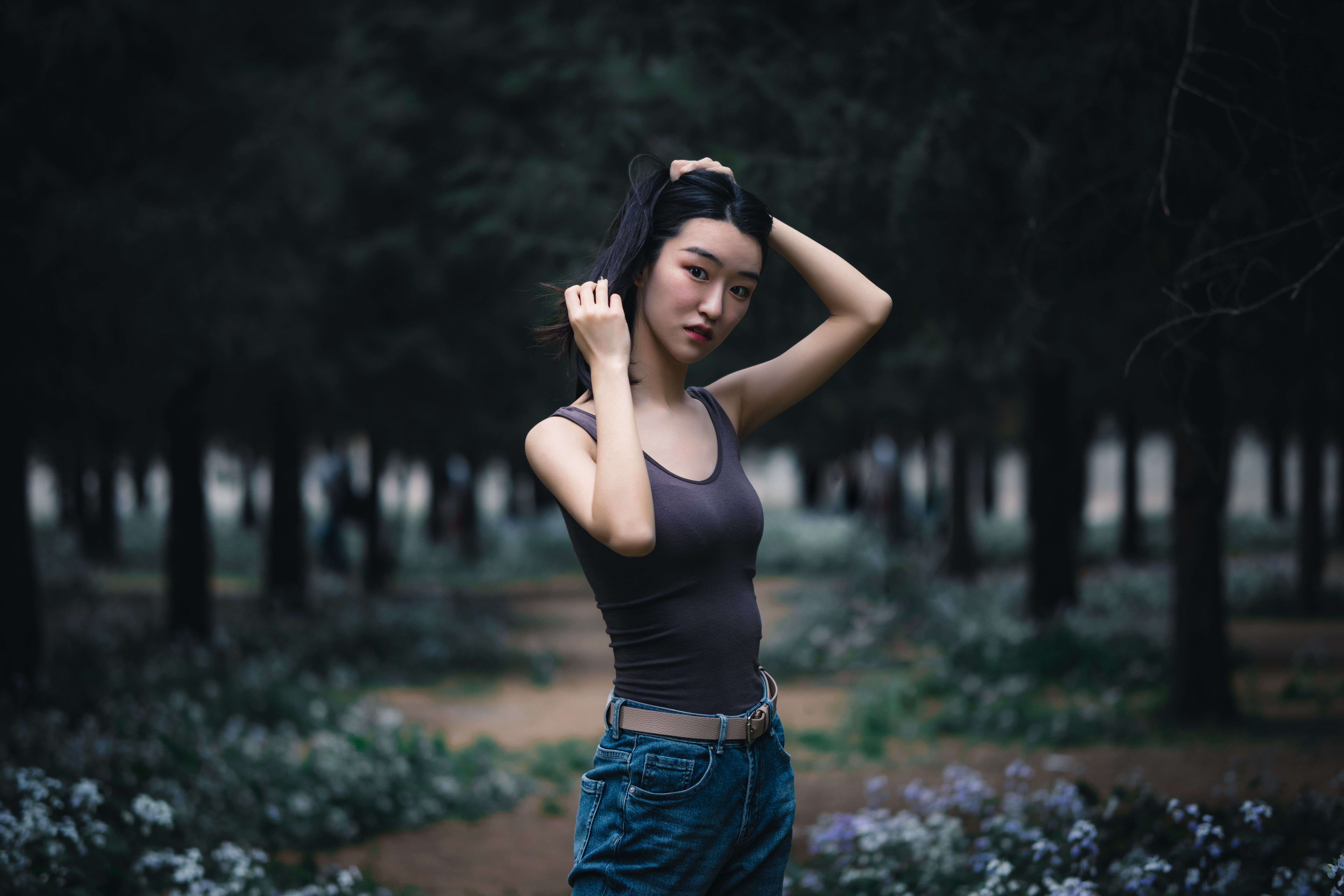 一名年轻女子站在一片宁静的森林中，周围郁郁葱葱的绿色植物环绕，她正沉思着