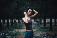 一名年轻女子站在一片宁静的森林中，周围郁郁葱葱的绿色植物环绕，她正沉思着