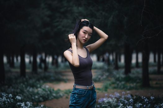 一名年轻女子站在一片宁静的森林中，周围郁郁葱葱的绿色植物环绕，她正沉思着