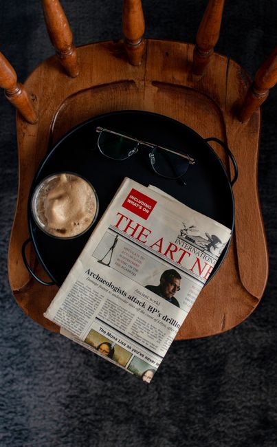 Overhead view of coffee, newspaper, and glasses on a wooden chair, perfect for lifestyle themes.