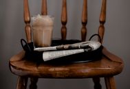 Foamy coffee and newspaper served on tray placed on chair