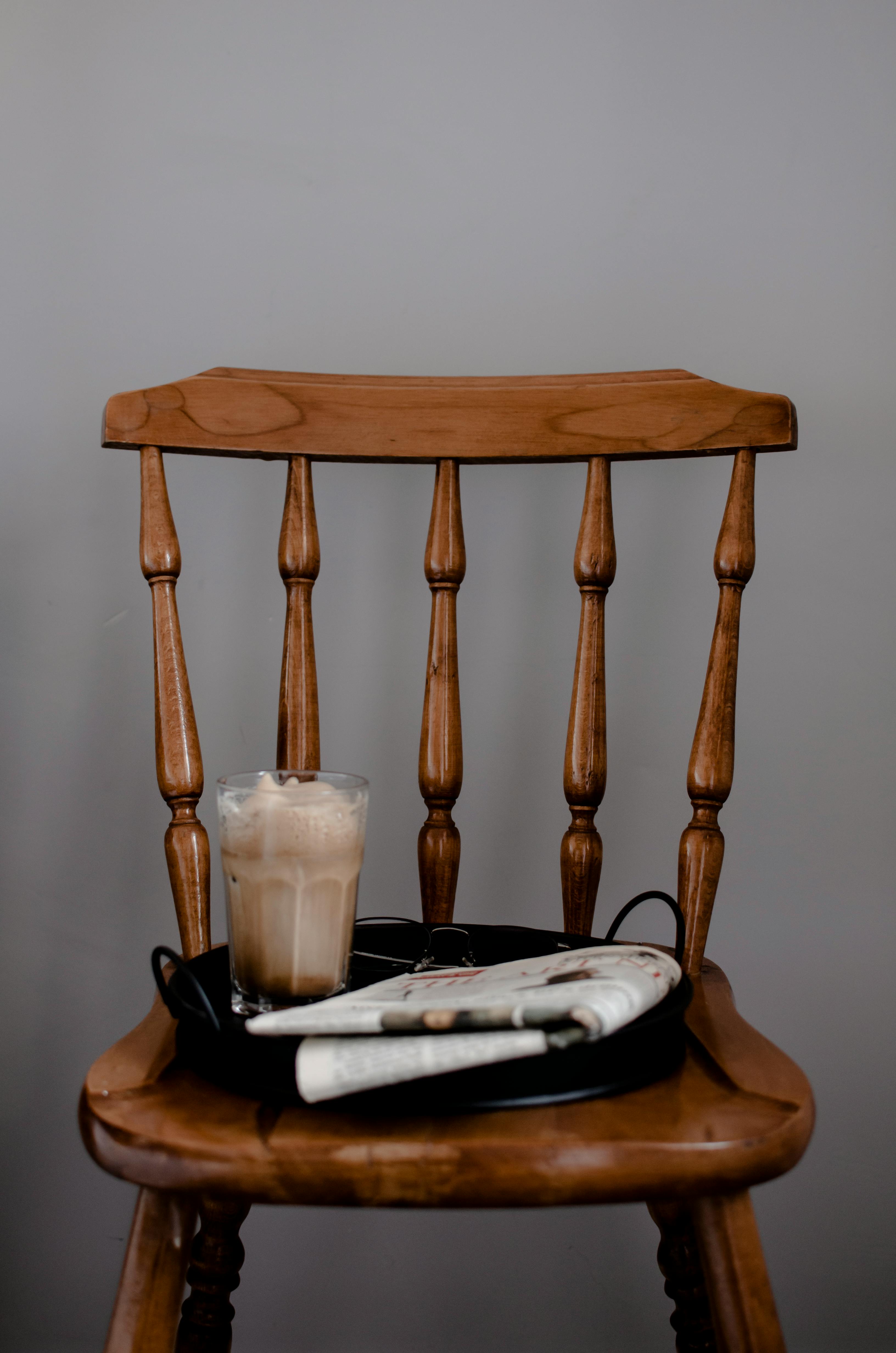 newspaper and coffee placed on wooden chair against gray background