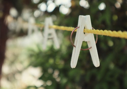 Closeup of white clothespins on yellow laundry rope hanging in courtyard near green trees