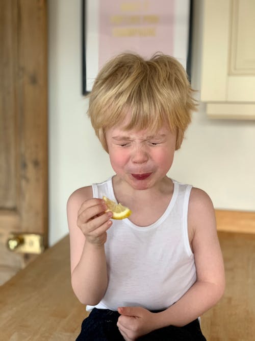 Free Adorable little child closing eyes while biting lemon Stock Photo