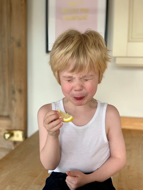 Adorable little child closing eyes while biting lemon