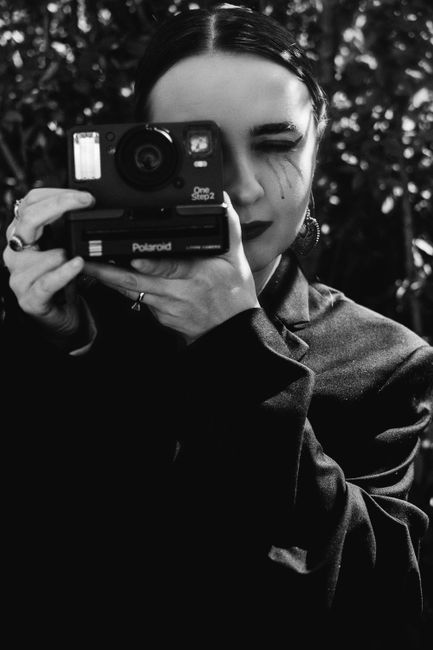 Black and white portrait of a woman holding a Polaroid camera capturing a timeless vintage feel.