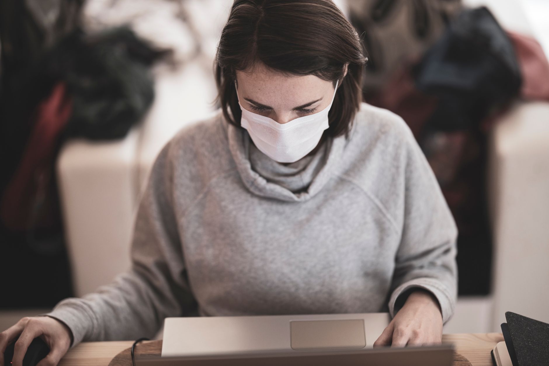 Woman wearing a facemask using a laptop at home, embracing remote work.