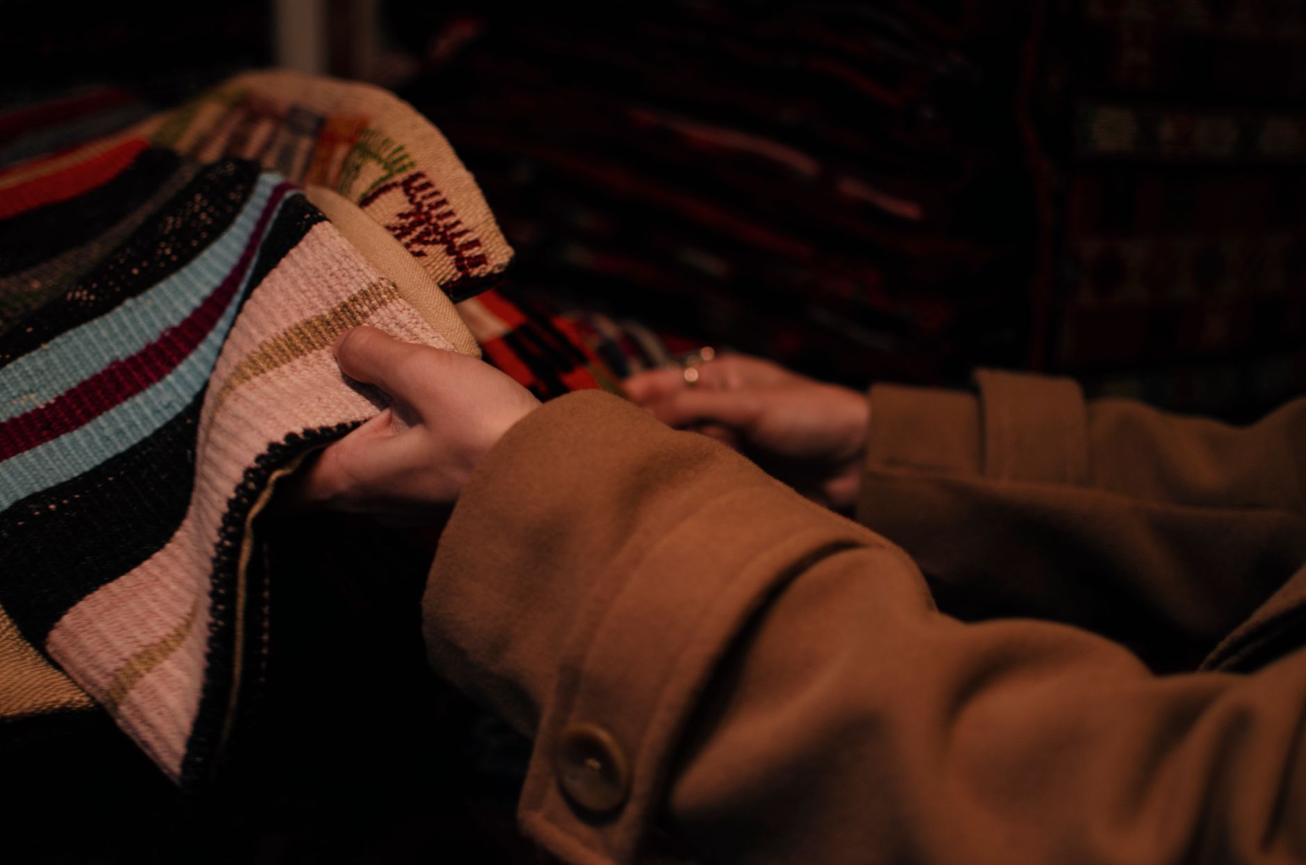 訂製窗簾一窗一價合理嗎?教你一步步判斷 A woman examines colorful textiles in a dimly lit store, highlighting fabric selection.