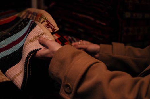 From above of crop anonymous female wearing warm clothes choosing knitwear in shop