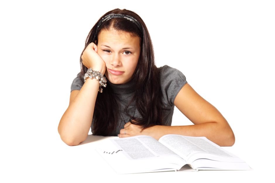 Student resting her head on her hand, looking tired and unmotivated while studying from a textbook