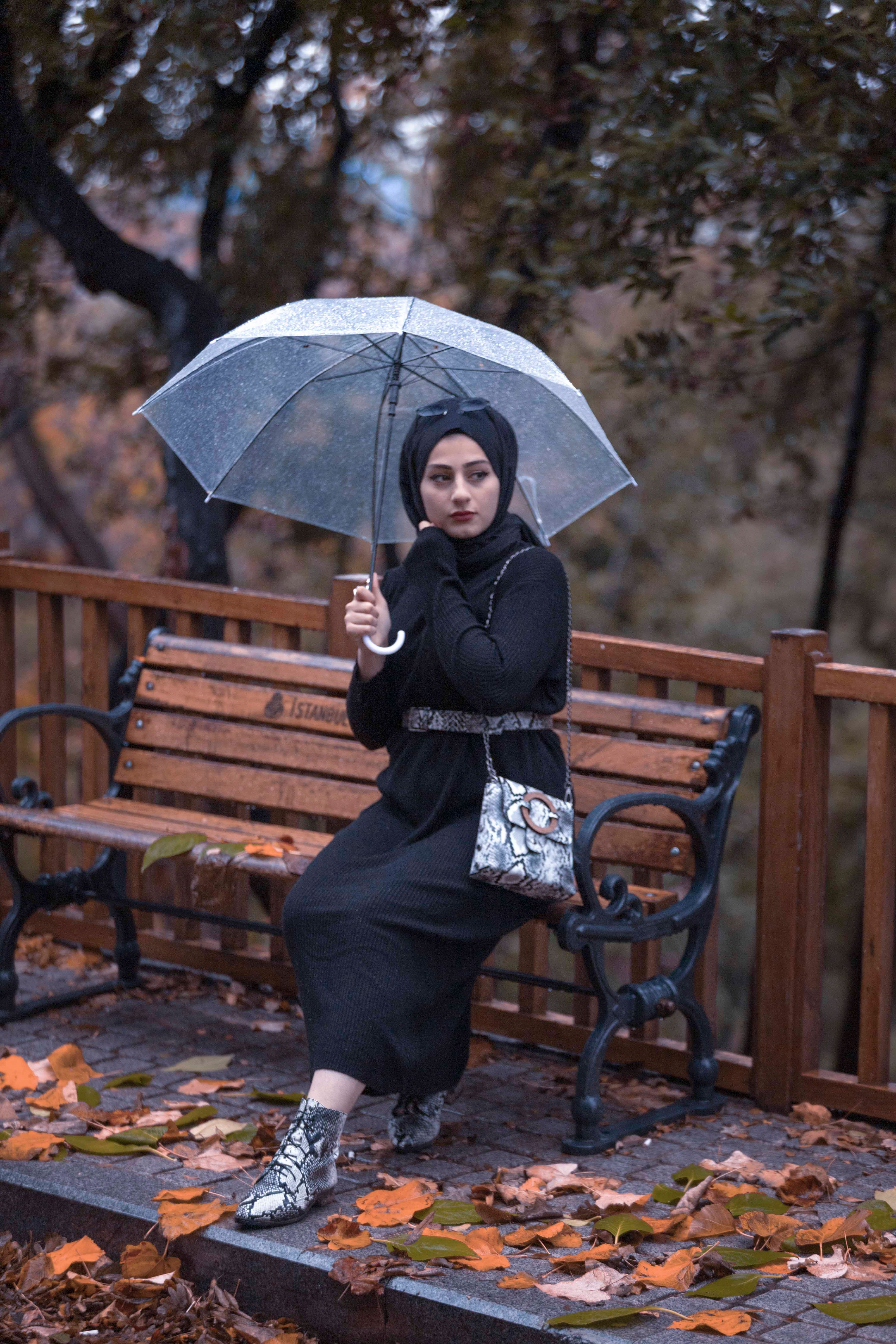 一位戴头巾的女人坐在一把带雨伞的长椅上，享受着宁静的秋日