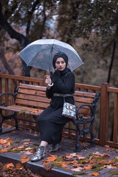 一位戴头巾的女人坐在一把带雨伞的长椅上，享受着宁静的秋日