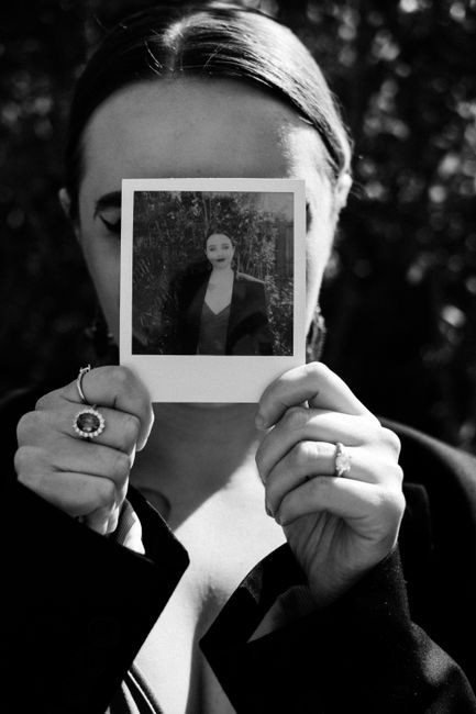 Black and white of female in rings with precious stones covering face with instant photography in sunlight