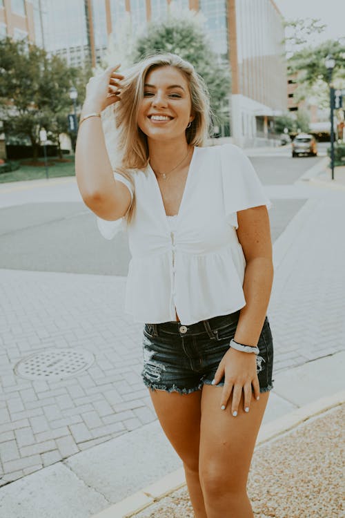 Smiling young female in summer outfit standing on pavement and enjoying sunny summer day in city