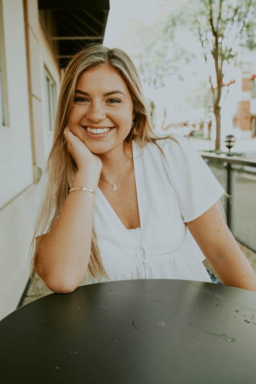 Free Happy young female leaning on hand while sitting at table in outdoor cafeteria Stock Photo