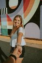 Cheerful young female in casual outfit smiling happily while holding hand of boyfriend during free time together