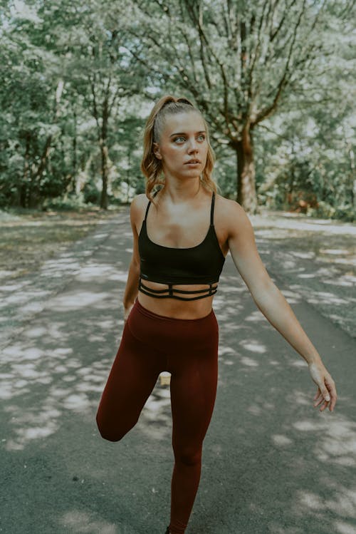 Confident young female athlete stretching leg while warming up before workout in sunny park