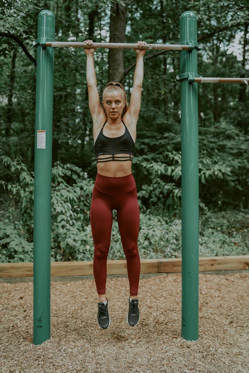 Full body of muscular young woman hanging on horizontal bar while training in sports ground