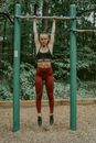 Full body of muscular young woman hanging on horizontal bar while training in sports ground