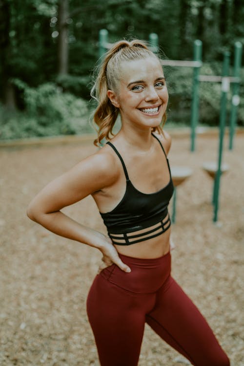 Positive young sportswoman in activewear smiling at camera while resting during training in park