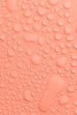 Plain light peach colored background with transparent water drops of different sizes and shapes flowing down and placed close to each other