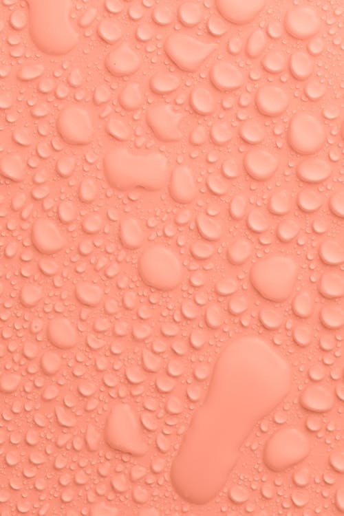 Plain light peach colored background with transparent water drops of different sizes and shapes flowing down and placed close to each other
