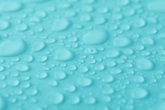 Macro shot of water droplets on a vibrant turquoise surface, showcasing texture and clarity.