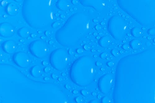 Closeup top view of dark blue wet blurred background with still shiny abstract transparent fluid drops of different sizes and shapes
