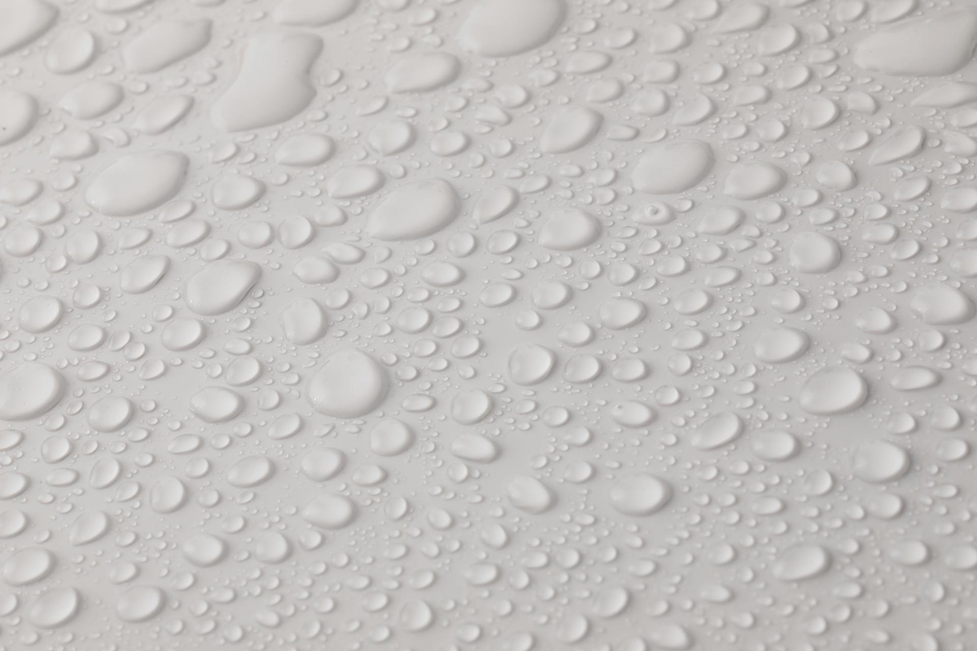 Closeup top view of plain wet abstract surface with small dripped water drops of different shapes placed on white background