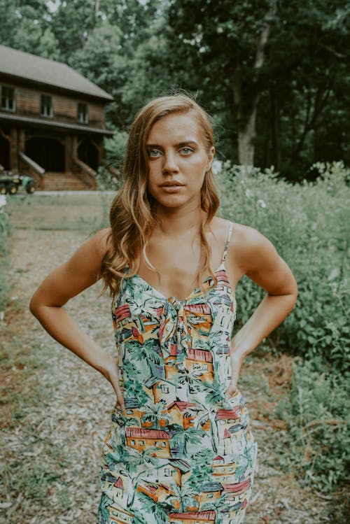 Confused young woman with hands on waist looking at camera while standing in green yard