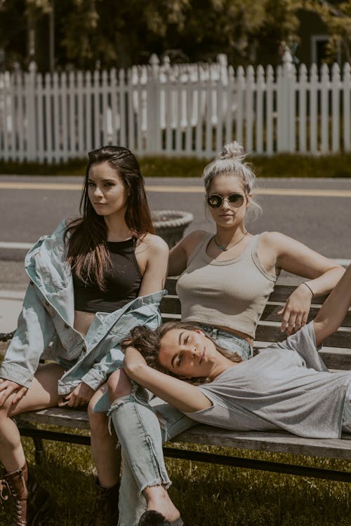 Group of young females in casual modern clothes relaxing together on bench near road