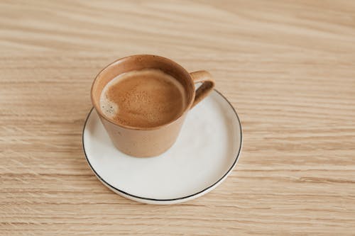 Free From above of beige ceramic cup of aromatic espresso on white elegant saucer with thin black edge placed on wooden surface Stock Photo