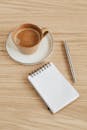 从打开的笔记本上方，用白纸靠近银笔，木桌上的香杯里盛着热浓缩咖啡