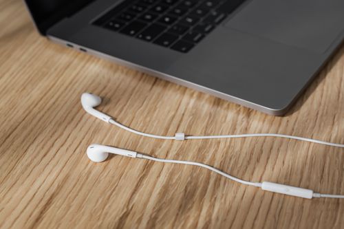 Free From above composition of contemporary white wired earphones placed near gray colored modern laptop keyboard on wooden desk in daylight Stock Photo