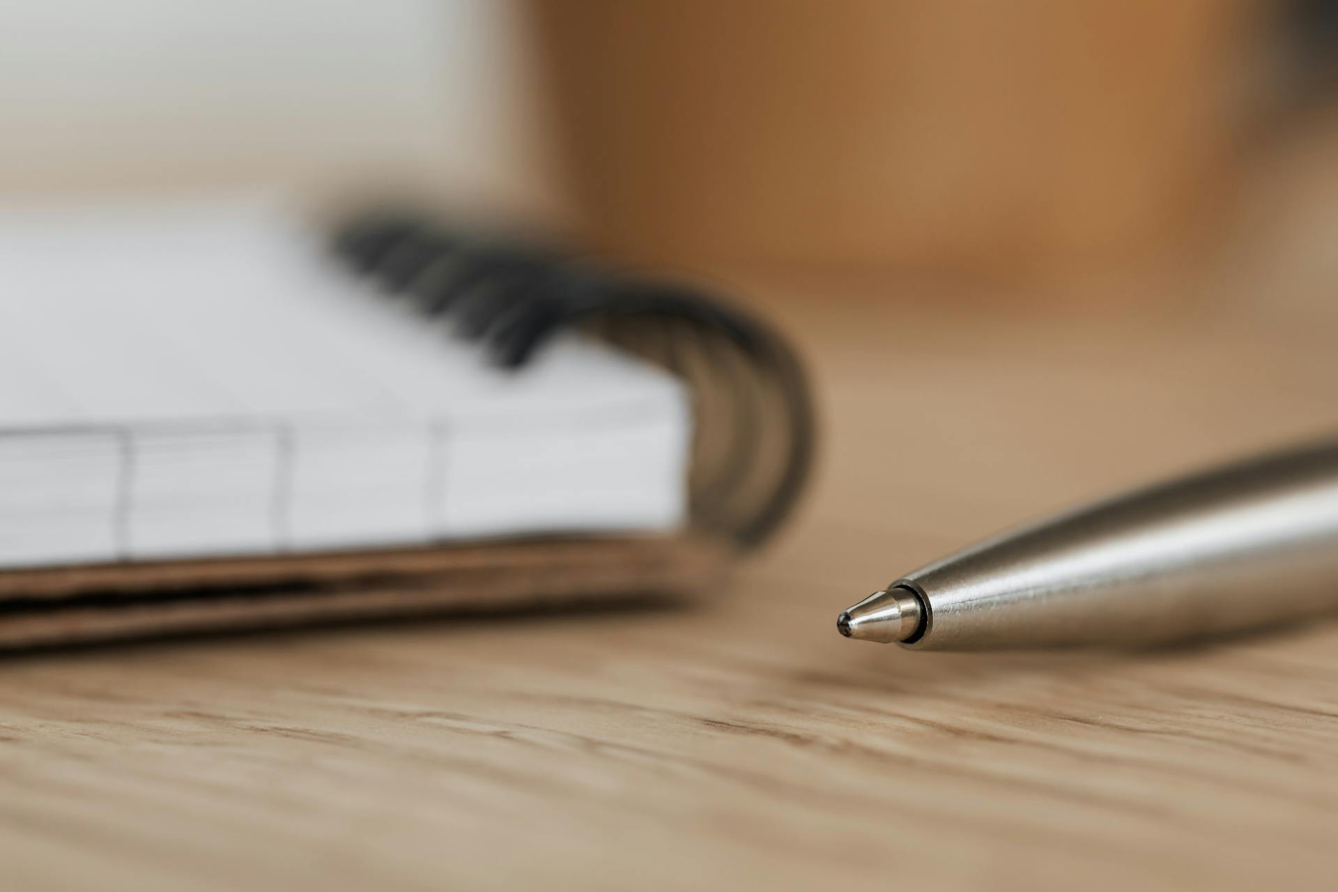 Side view closeup of opened ring bound notebook with blank pages near silver ball point pen placed on wooden table