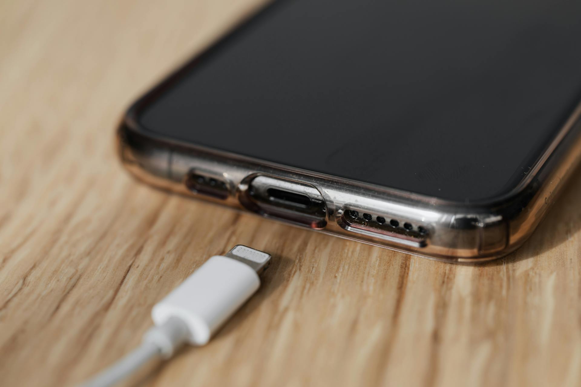 Modern cellphone in transparent cover with closeup of charging input and mobile phone white charger cable usb connector on wooden table