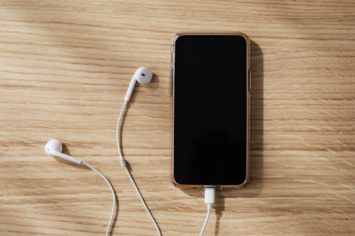 Charging smartphone and white earphones on wooden table