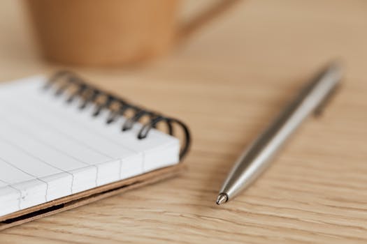 A detailed close-up photograph of a notepad and pen resting on a wooden desk.