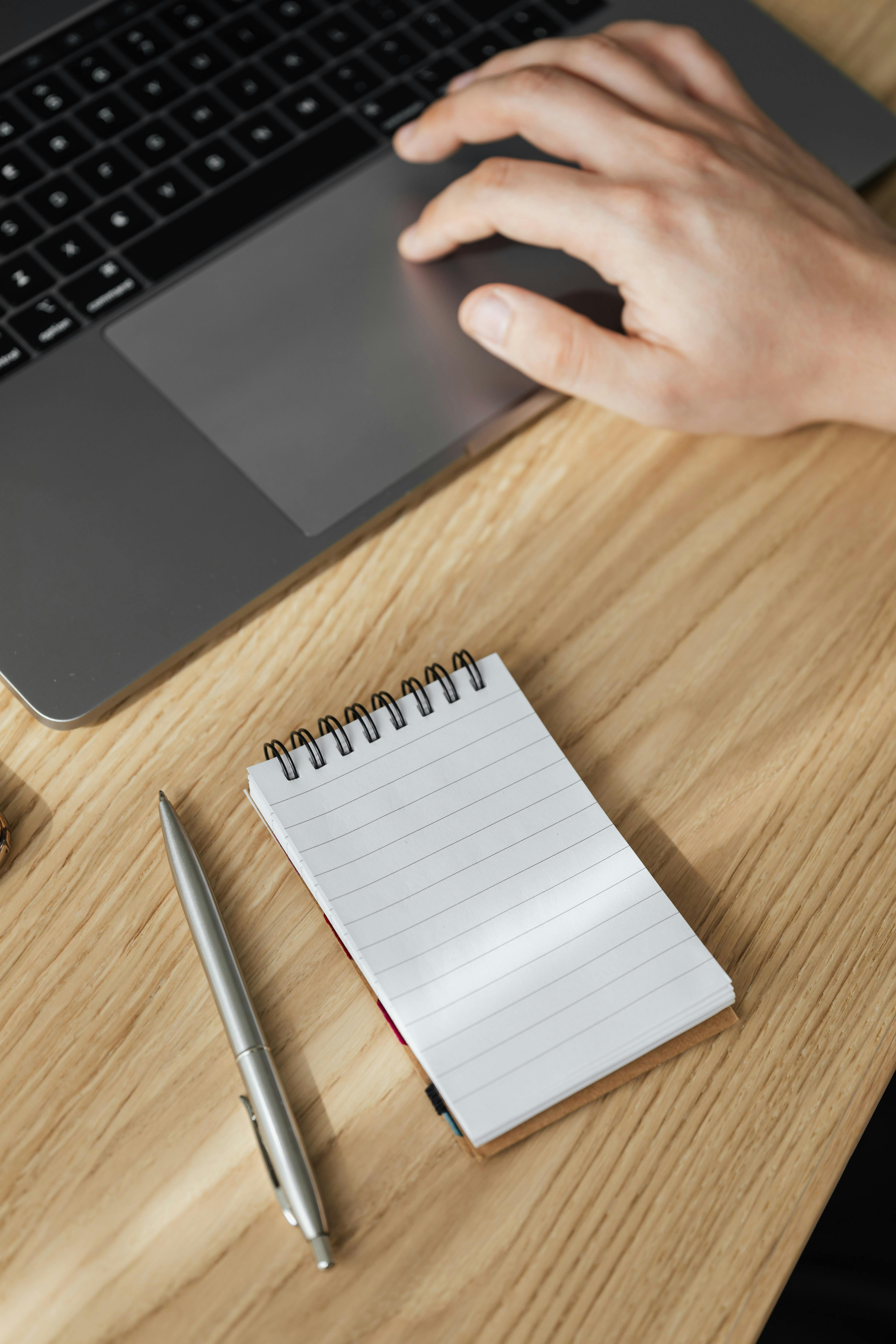 crop man using touchpad on laptop and notebook with pen